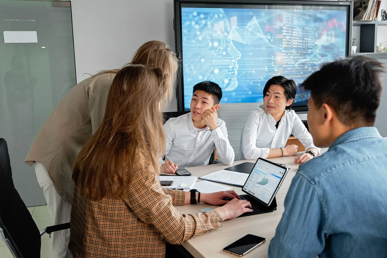 A team collaborating around a table with laptops and a screen